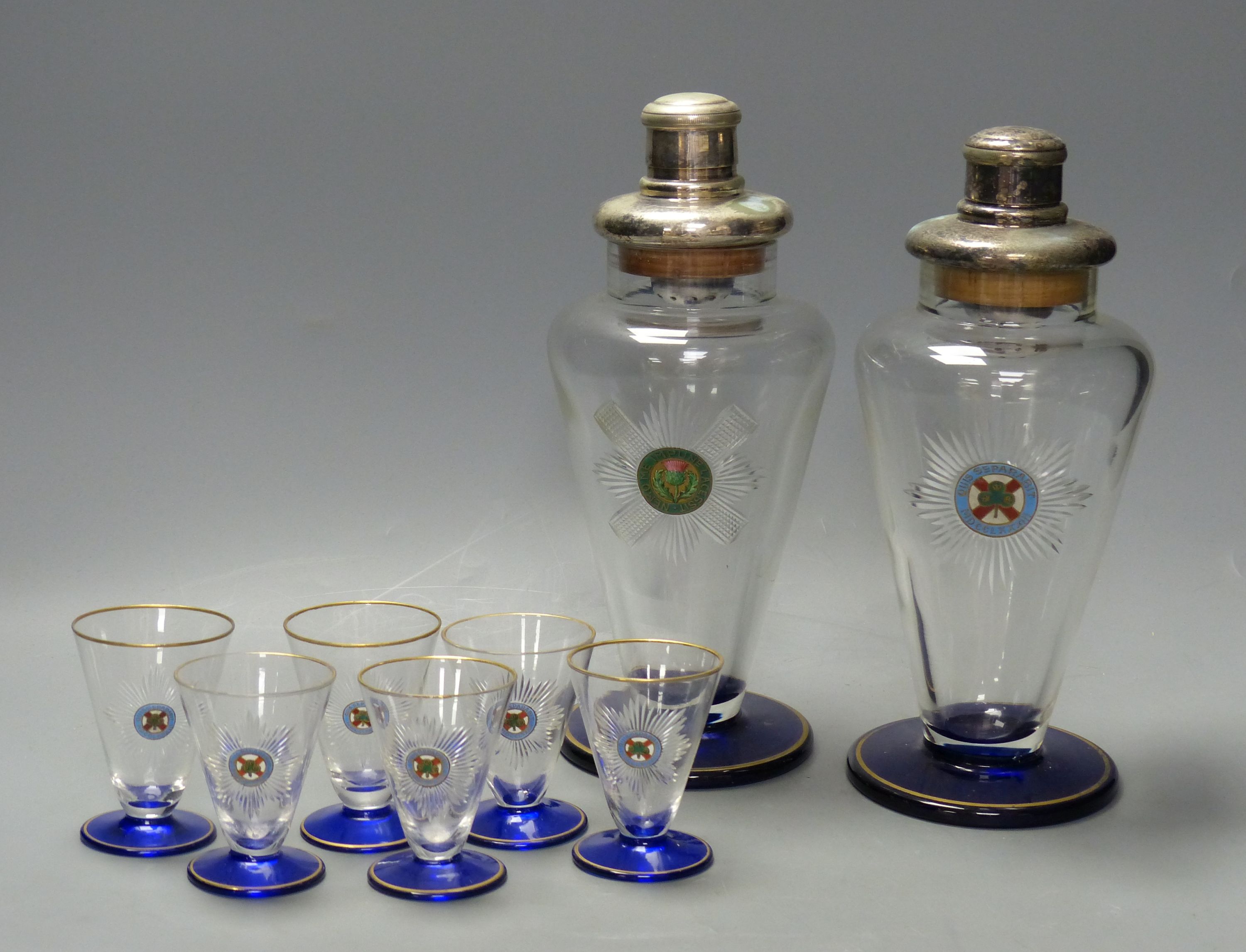 A pair of Art Deco cobalt blue and gilt-mounted tapered glass cocktail shakers, c.1920, enamelled with Black Watch and 4th Royal Irish Dragoon Guards mottos and six matching glasses